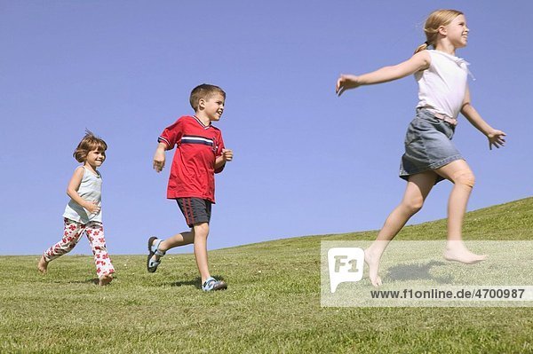 Three children running along a hillside.