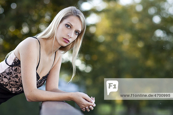 Portrait of a young woman with long blond hair leaning on bridge railings