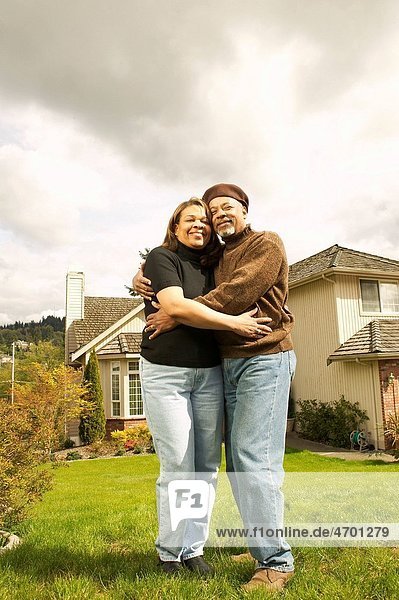 A couple hugging in front of their home.