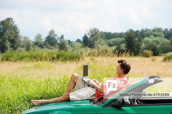 Man on car hood using laptop