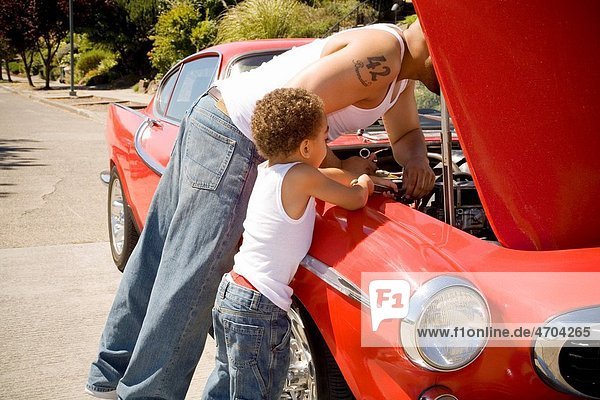 Father and son checking under car hood