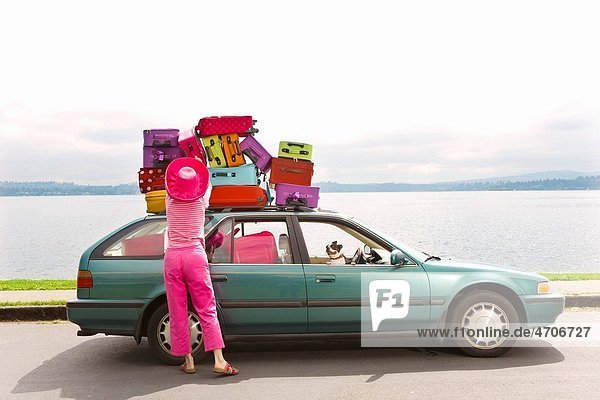 Woman adjusting stack of colorful suitcases on top of car