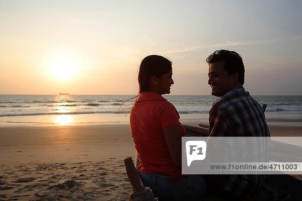 South Asian Indian young man and woman sitting close to each other in the evening on seashore Shiroda Dist Sindhudurga Maharashtra India MR703D 703E