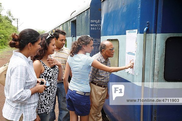 Travel group searching their names on reservation chart fixed near door of long distance train MR468