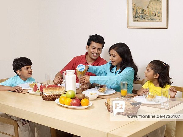 Mother pouring juice in glass with family sitting on dining table for breakfast MR702R MR702S MR702T MR702U