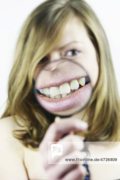 Young woman with magnifying glass in front of her teeth  mouth