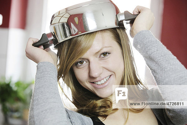Junge Frau in der Küche mit Kochtopf als Hut
