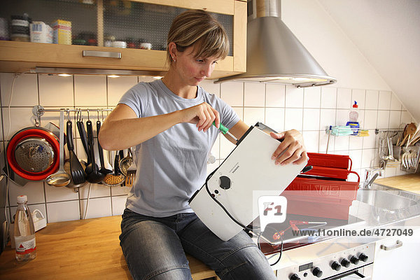 Junge Frau repariert einen Toaster in einer Küche