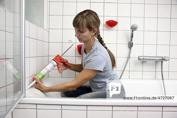 Young woman sealing joints with a plastic composition and the help of a sealant gun in a bathroom