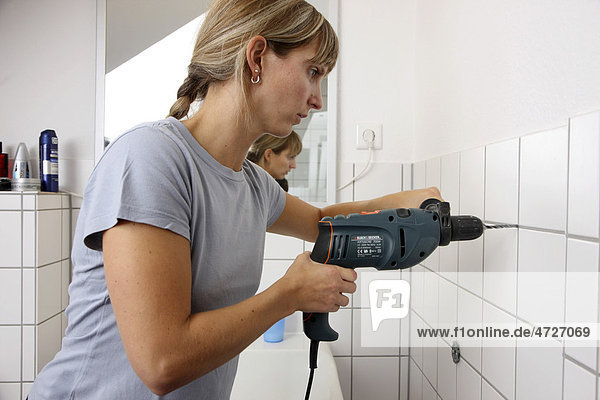 Young woman drilling a hole in a tiled bathroom wall