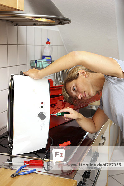 Young woman repairing a toaster in the kitchen