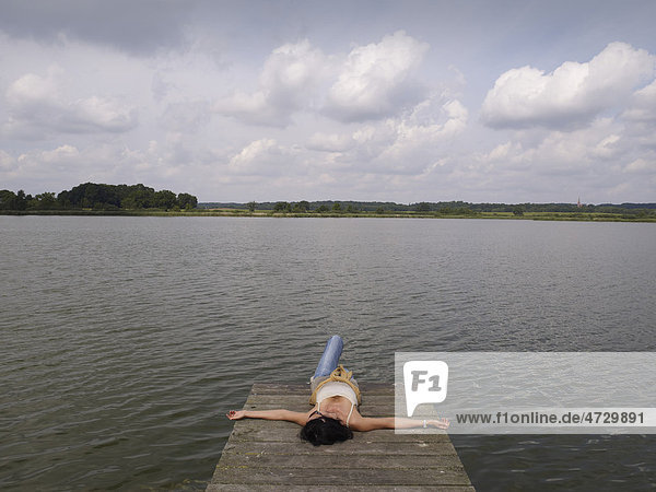 Frau entspannt sich liegend auf einem Holzsteg an einem See der Mecklenburgischen Seenplatte  Mecklenburg-Vorpommern  Deutschland  Europa