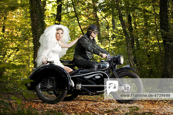 Braut und Bräutigam fahren in Motorrad mit Beiwagen zur Hochzeit