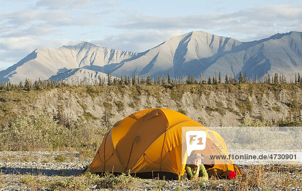 Young woman looking out of an expedition tent  arctic tundra  camping  Mackenzie Mountains behind  Wind River  Yukon Territory  Canada