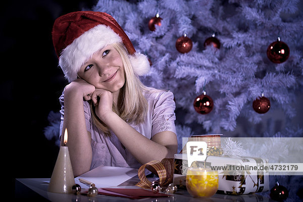 Ein Mädchen mit Weihnachtsmannmütze schreibt Weihnachtspost am Weihnachtsbaum