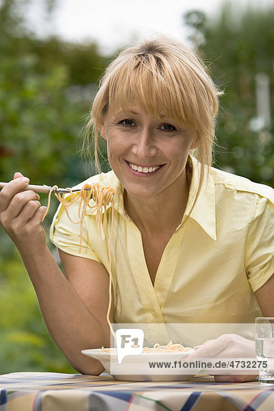 Frau isst Spaghetti im Garten