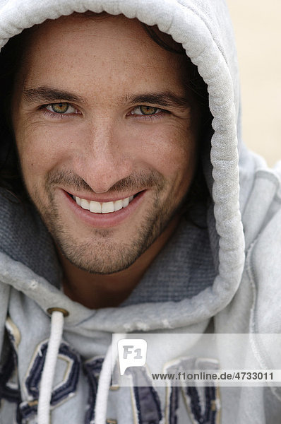 Mann Anfang dreißig in Kapuzensweatshirt bei schlechtem Wetter am Strand,  Portrait
