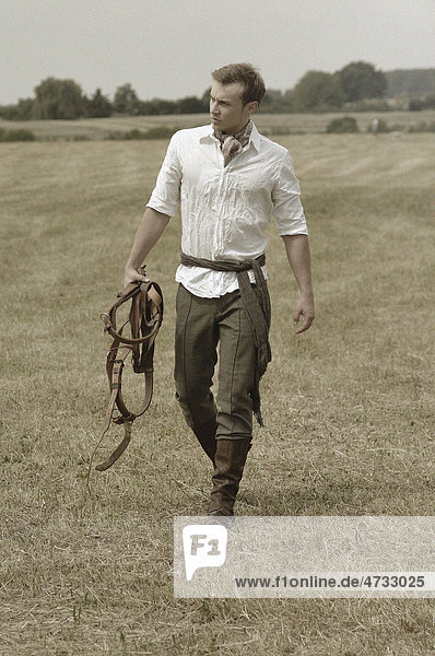 Man wearing riding clothes walking in a field in summer