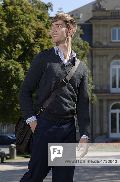 Young man wearing elegant clothing with a bag over his shoulder in front of the New Palace in Stuttgart  Baden-Wuerttemberg  Germany  Europe