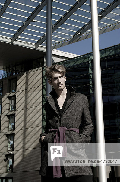 Young man wearing an overcoat in front of modern architecture  fashion shoot