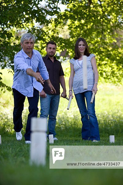 Drei Erwachsene spielen Kubb auf Gras