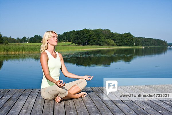 Young woman meditating on jetty