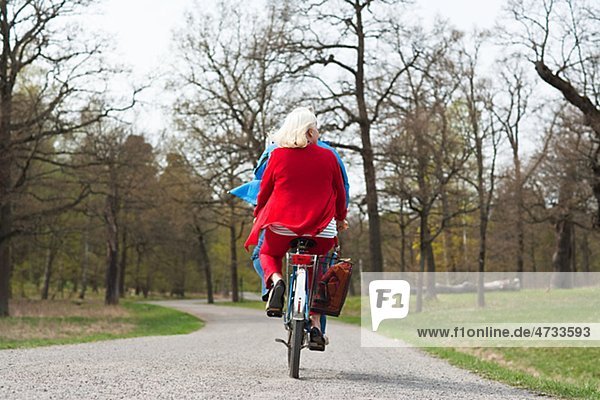 Senior couple riding tandem bike in park