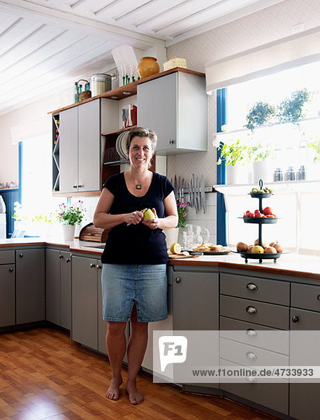 Mature woman standing in kitchen  peeling apple