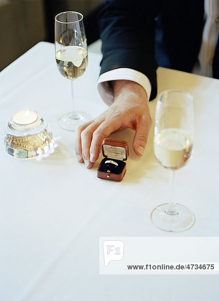 Mans hand reaching engagement ring on table with wine