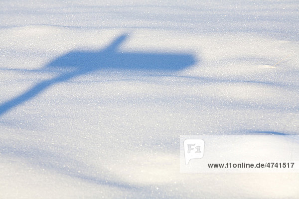 Schatten eines Wegweisers auf Schnee