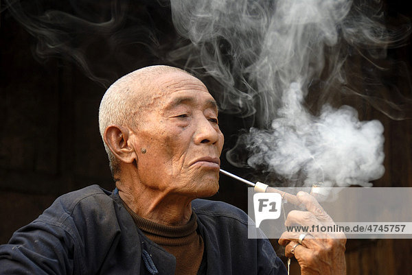 Male smoker  portrait  indulgence  old man of the Mouchi ethnic group smoking a pipe  smoke lingering in the air  Ban Mouchi Kaw village  Samphan district  Phangsali or Phongsaly Province  Laos  Southeast Asia  Asia