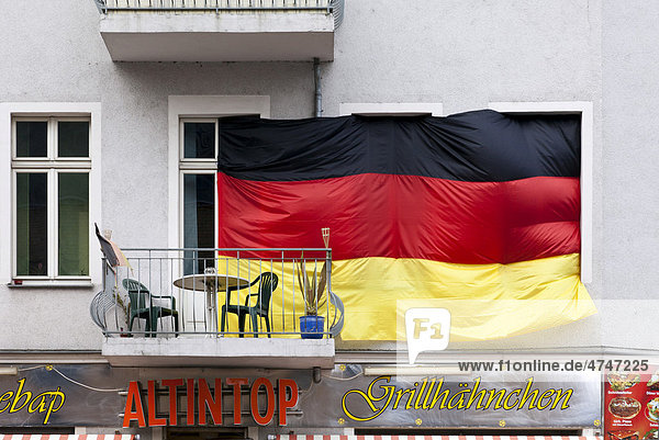 Riesige Deutschlandfahne verdeckt die Fenster zu einer Wohnung  mit Balkon  darunter Imbiss mit Grillhähnchen  Oberschöneweide  Berlin  Deutschland  Europa