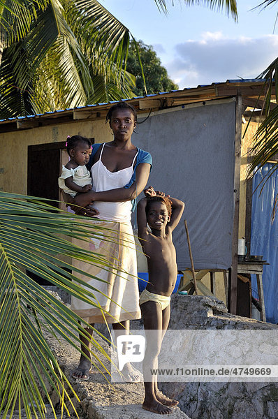 Mother with children standing in front of an earthquake-proof prefabricated house  provided to her by an aid organization  Petit Goave  Haiti  Caribbean  Central America
