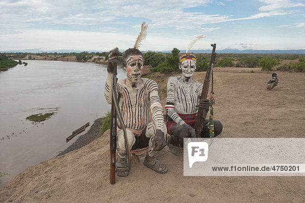 Two Karo warriors with body and facial paintings and rifle seated on their headrest  Omo river valley  Southern Ethiopia  Africa