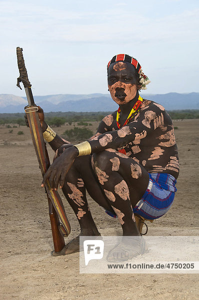 Karo Krieger mit Körperbemalung und Gesichtsbemalung und einem Gewehr sitzt auf seiner Kopfstütze  Omo-Tal  Südäthiopien  Äthiopien  Afrika