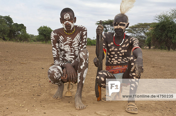 Zwei Karo Krieger mit Körperbemalung und einem Gewehr sitzen auf ihrer Kopfstütze  Omo-Tal  Südäthiopien  Äthiopien  Afrika