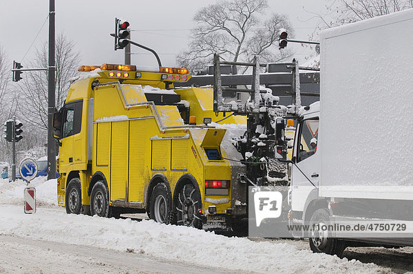 Winter  Lastkraftwagen wird von großem Abschleppwagen auf schneebedeckter Straße abgeschleppt