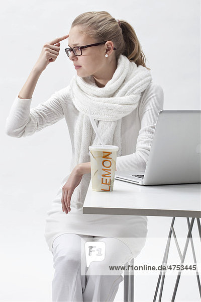 Blonde  weißgekleidete junge Frau neben einem Laptop