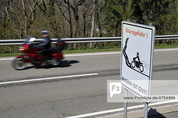 Motorcyclist on a country road with a warning sign  Sturzgefahr - Rasen ist out  German for dangerous curves - no speeding  Eifel  Germany  Europe