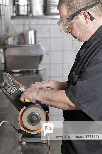 Koch schleift Messer auf Bandschleifmaschine in Küche