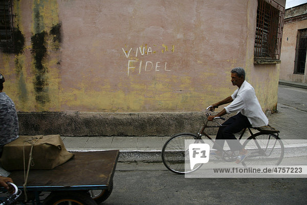 Fahrradfahrer vor einem Viva Fidel Schriftzug in Holguin  Kuba