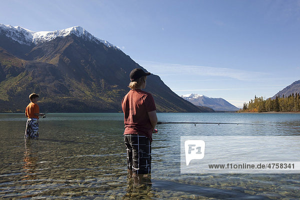 Children  young boys  standing in shallow water  fishing at Kathleen Lake  King's Throne behind  St. Elias Mountains  Kluane National Park and Reserve  Yukon Territory  Canada