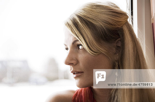 Junge Frau guckt traurig aus dem Fenster  Porträt