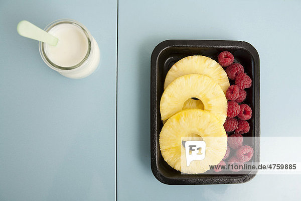 Packaged pineapple slices and raspberries with a tub of yoghurt