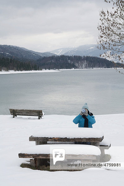 Frau trinkt aus einer Flasche am Walchensee Picknicktisch Winter Bayern Deutschland Europa