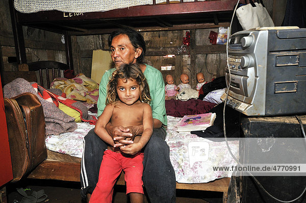 Mother  43  and daughter  8  sitting on a bed in their humble shack in a Favela or shanty town  the family lives by collecting  separating and selling recyclable waste  satellite city of Ceilandia near Brasilia  Distrito Federal  Brazil  South America