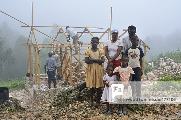 Eine Familie  Opfer des schweren Erdbebens im Januar 2010  neben ihrem neue erdbebensicheren Haus mit Fachwerkstruktur  das von einer deutschen Hilfsorganisation zur Verfügung gestellt wird  Dorf Coq Chante nahe Jacmel  Haiti  Karibik  Zentralamerika