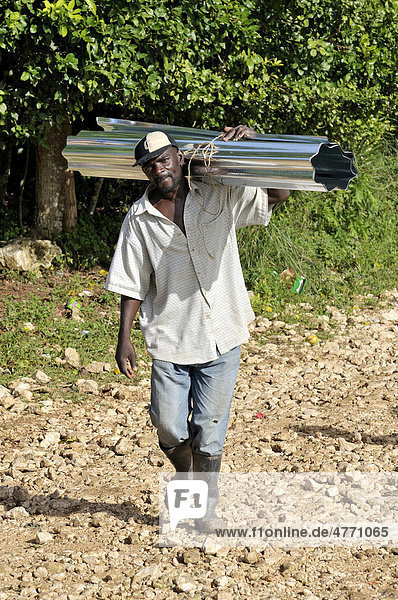 Mann trägt Wellblech für die Dachdeckung. Nach dem schweren Erdbeben im Januar 2010 bildet eine deutsche Hilfsorganisationen lokale Bauarbeiter im Bau erdbebensicherer Häuser aus  Dorf Coq Chante nahe Jacmel  Haiti  Karibik  Zentralamerika