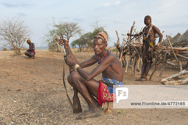 Hamar Krieger mit typischer Lehm Haarfrisur und mit Gewehr sitzt auf seiner Kopfstütze  Omo-Tal  Süd Äthiopien  Afrika