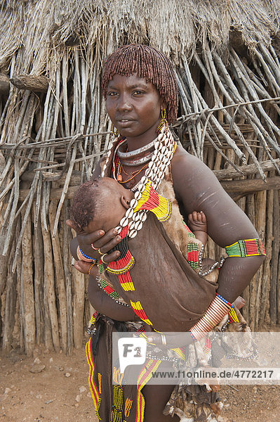 Junge Hamar Frau mit traditioneller Haarfrisur aus rotem Lehm und mit Halskette aus Kaurimuscheln hält ihr Baby im Arm  Omo-Tal  Süd Äthiopien  Afrika